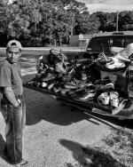 A man looks over his shoulder while a car full of junk in the road sits in front of him