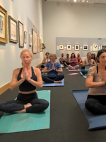 Yoga attendees in sitting in pose in art gallery.